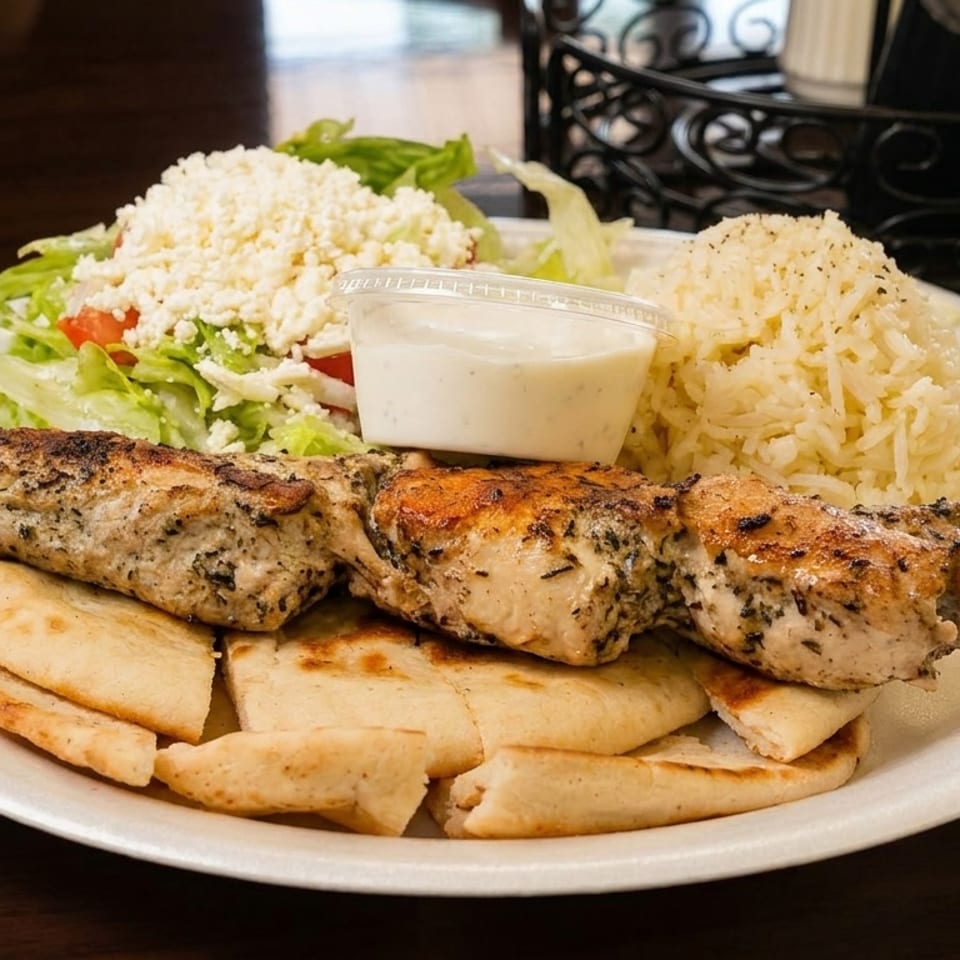 Chicken souvlaki skewer with pita bread, rice, salad with feta, and a side of tzatziki.