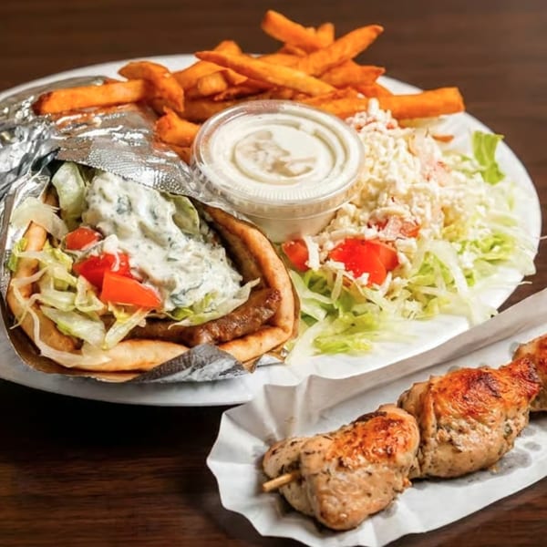 A gyro with fries, salad, and a side of chicken souvlaki on a white plate.