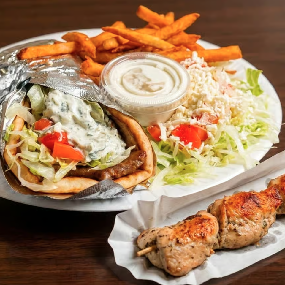 A gyro with fries, salad, and a side of chicken souvlaki on a white plate.