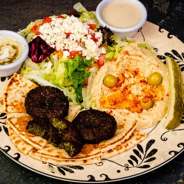 A colorful falafel platter with hummus, salad, pita bread, and two dipping sauces on a patterned plate.
