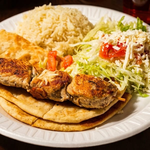 Chicken souvlaki skewer, rice, pita bread, and salad with feta on a white plate.