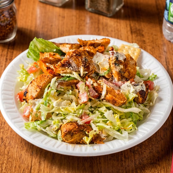 Grilled chicken salad with lettuce, tomatoes, and creamy dressing on a white plate.