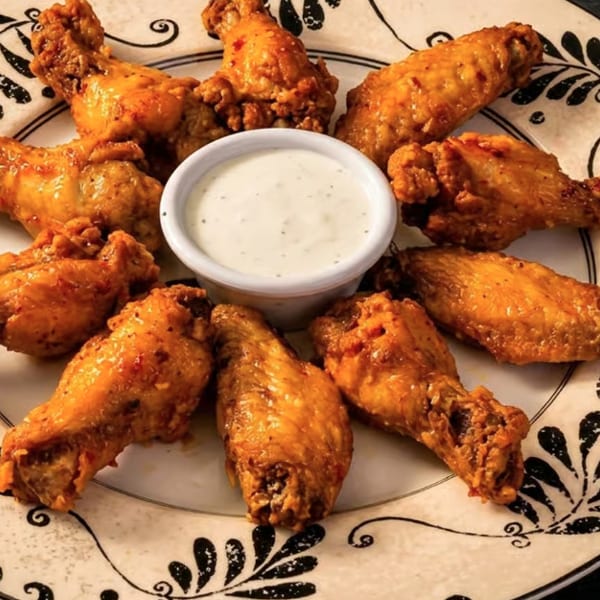 Crispy golden-brown chicken wings arranged in a circle around a small cup of ranch dressing on a decorative plate.