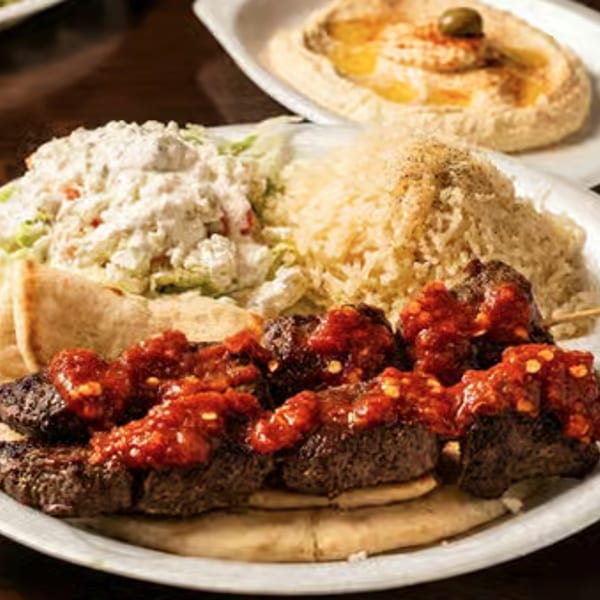 Spicy beef skewers with rice, salad, pita bread, and hummus on a white plate.