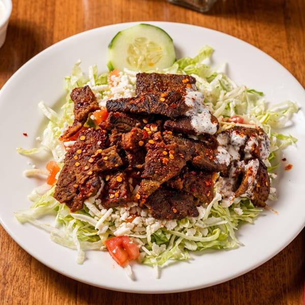 Spicy beef gyros with shredded lettuce, crumbled feta, diced tomatoes, and a cucumber slice.