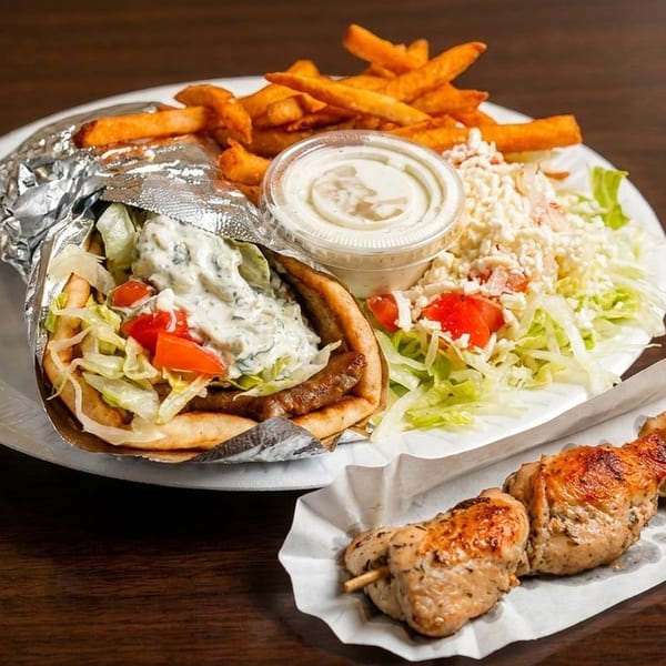 Gyro with fries, salad, and a chicken skewer on a white plate and paper tray.